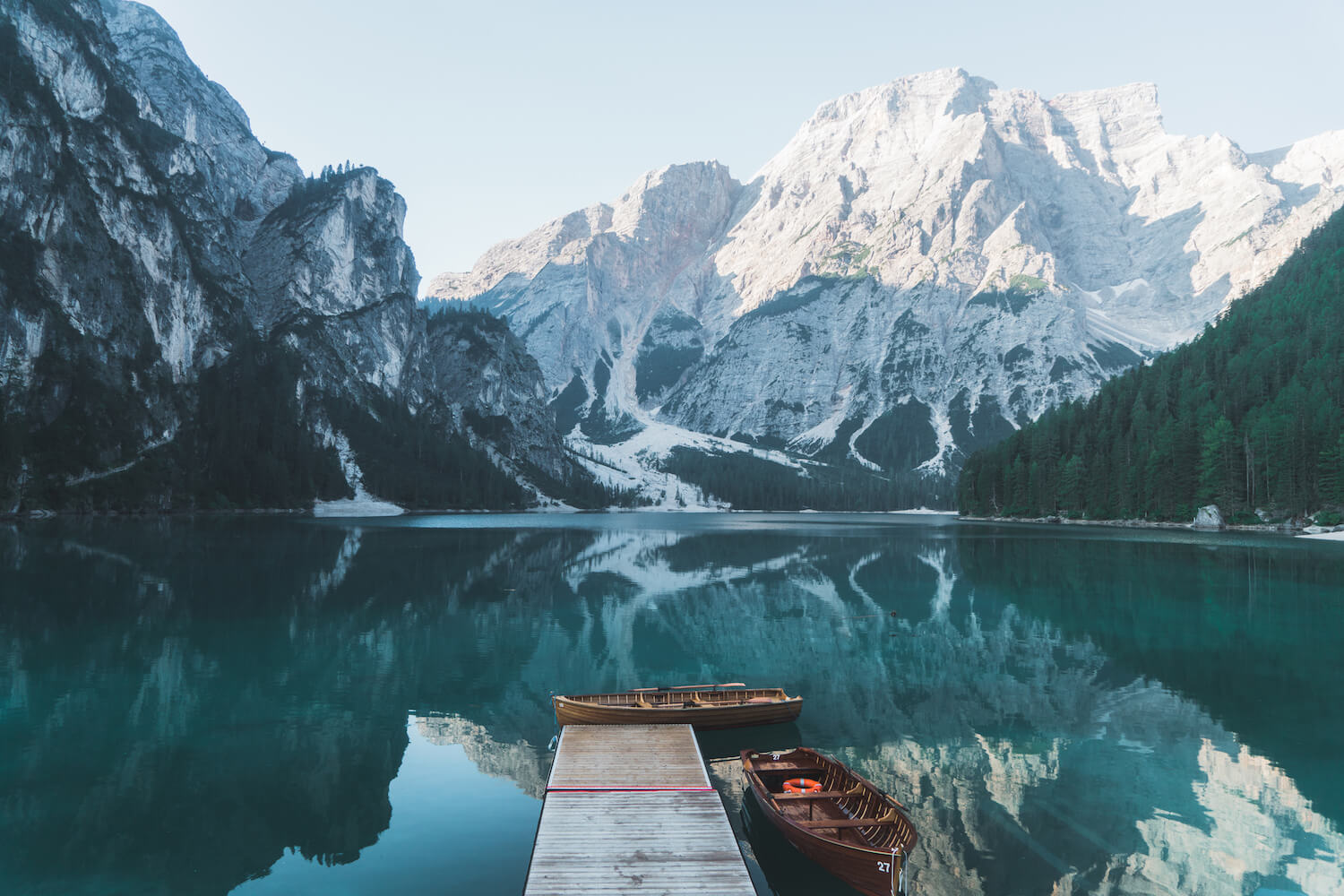 A beautiful mountain lake with a pier and two boats next to it. 