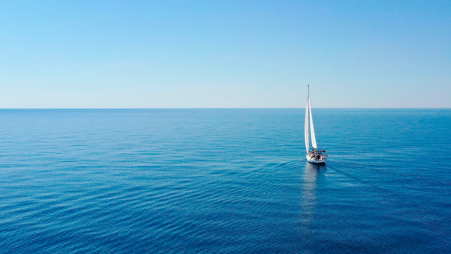 A calm sea with a sailing ship on it.