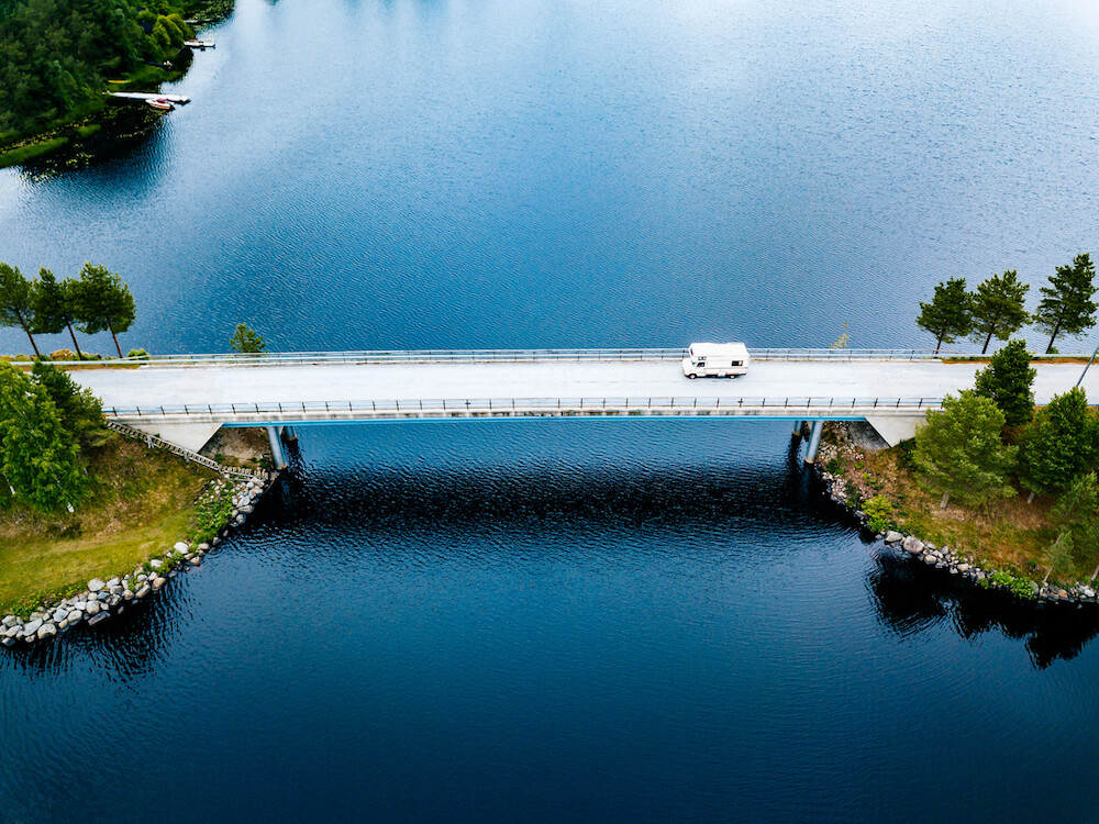 A bridge that connects two islands on a lake an a camper van drives over it. 