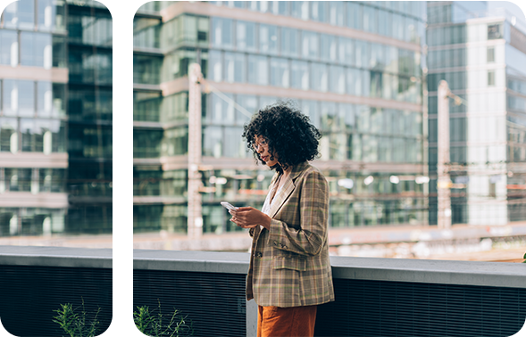 Modern gekleidete Frau unter Wolkenkratzern, die auf ihr Smartphone schaut