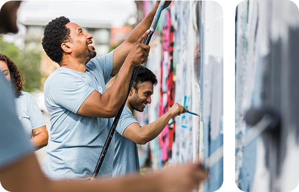 Person im blauen T-Shirt, die eine Wand streicht und lächelt.