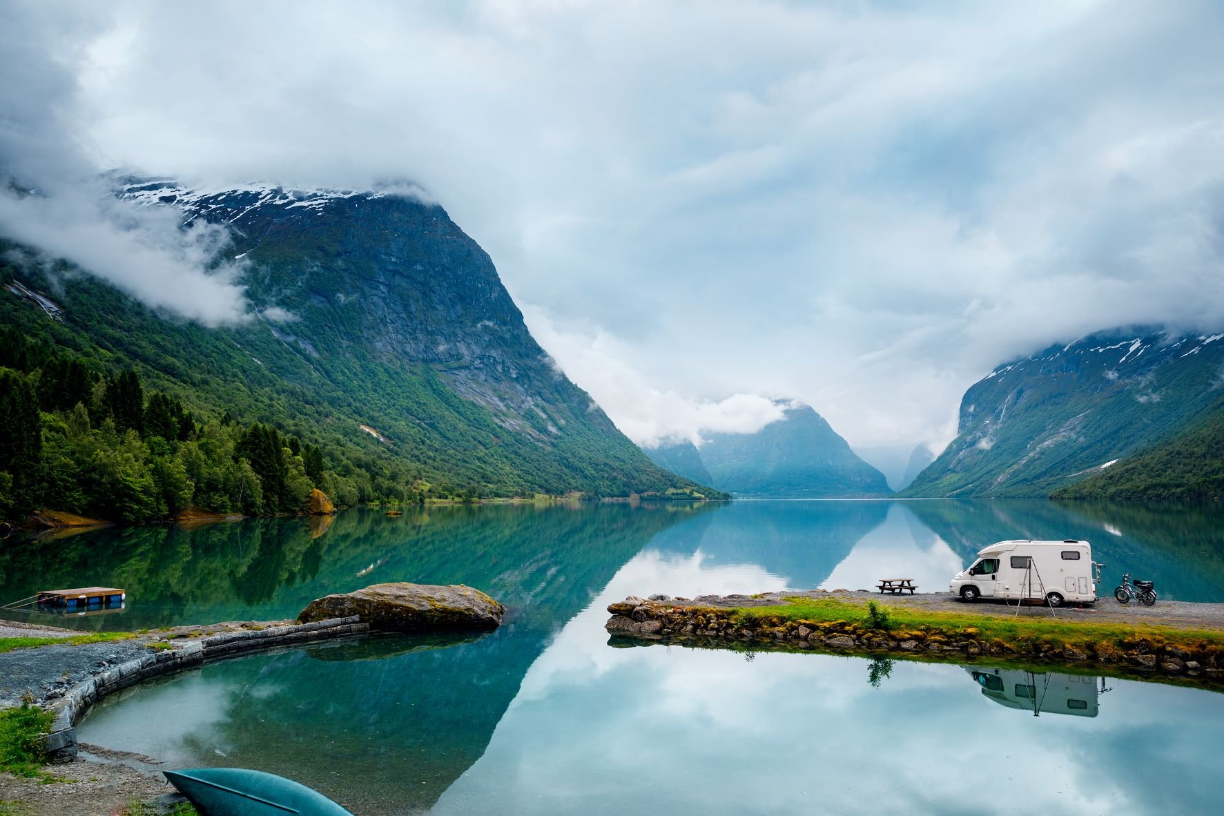 A blue mountain lake with a camper at the shore.