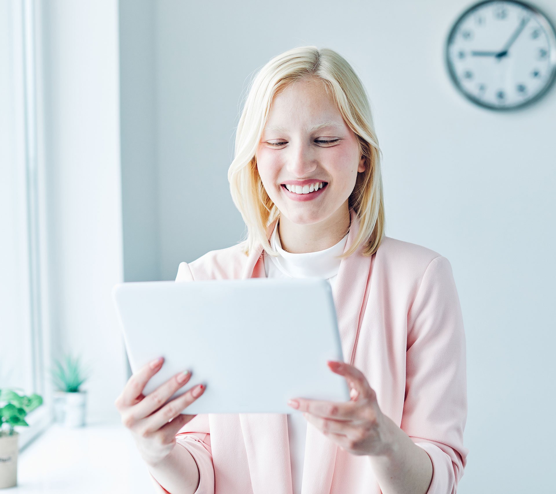 A young woman is smiling and holding a tablet.