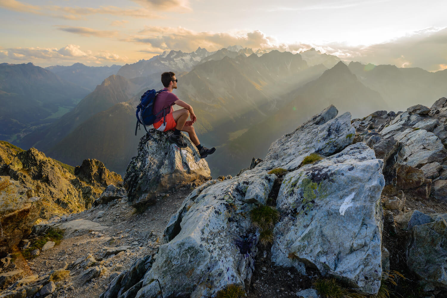 Ein Wanderer sitzt auf einem Fels und schaut auf die landschaft.